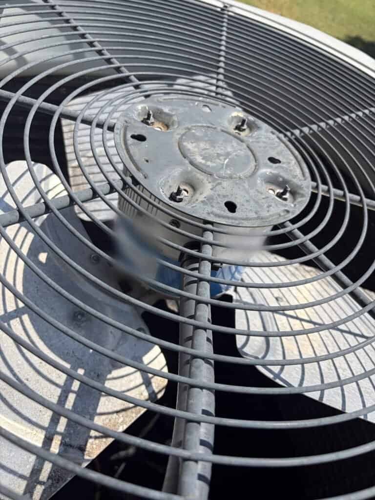 Replacement condenser fan motor installed under the fan guard of a Fort Smith AC unit