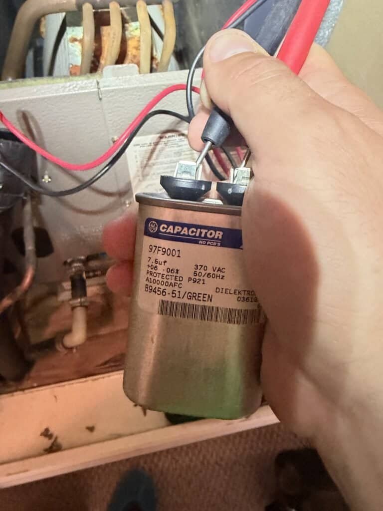 Technician testing an AC capacitor with meter leads during a Fort Smith tune-up