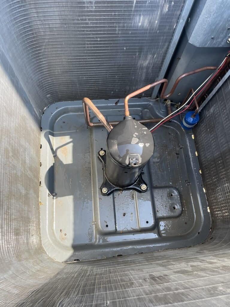 Inside a Fort Smith AC outdoor unit, showing the compressor and base pan during a tune-up