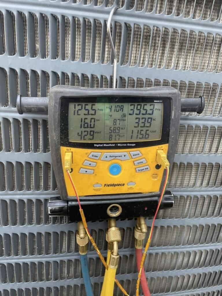 Digital refrigerant gauges hanging on a Fort Smith AC condenser during a tune-up