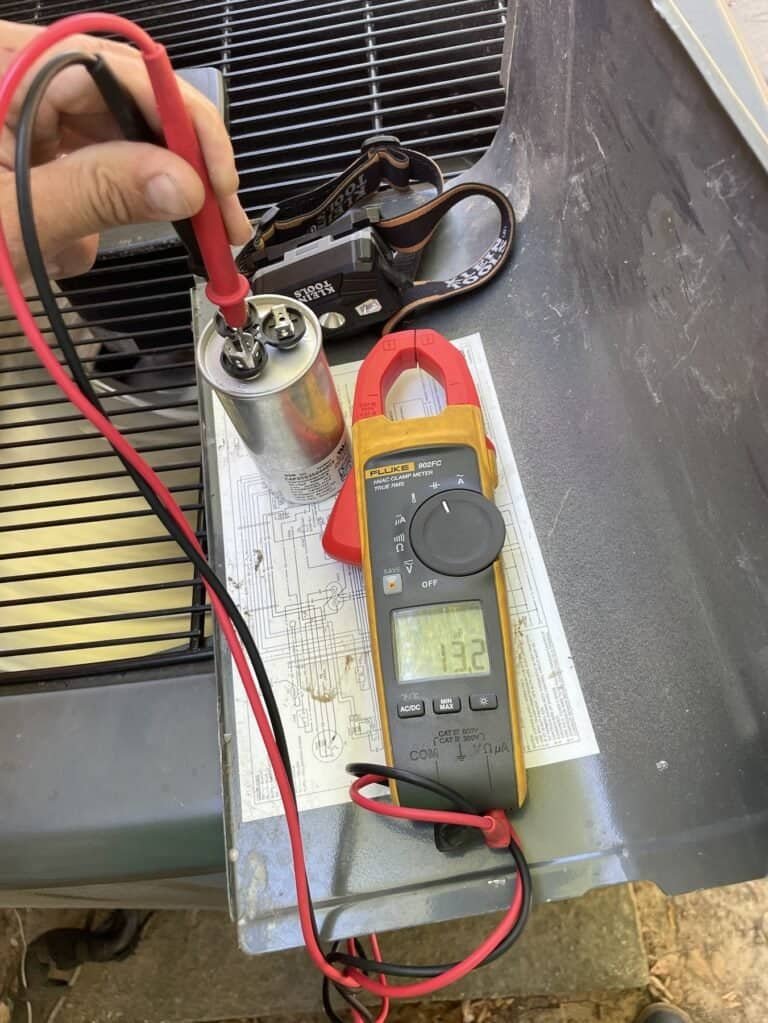 Technician testing an AC capacitor with a clamp meter on top of a Greenwood outdoor unit