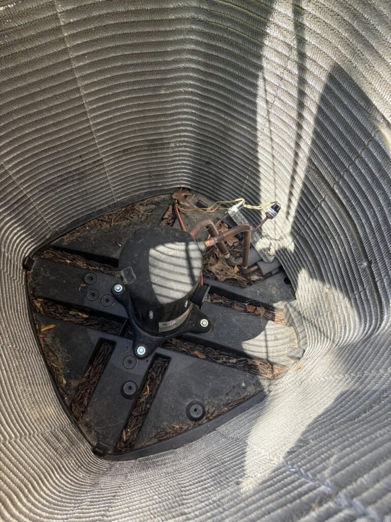 Leaves and debris in the bottom of an AC outdoor unit before cleaning in Rudy