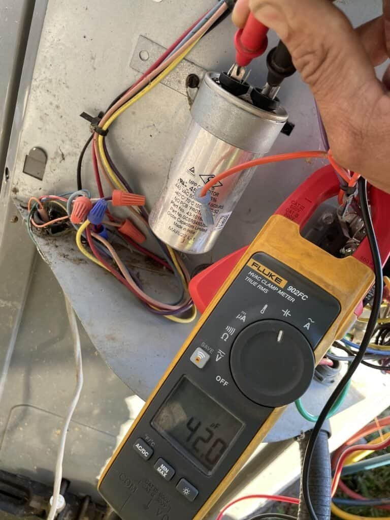 Technician testing a heat pump capacitor with a clamp meter at a Van Buren home