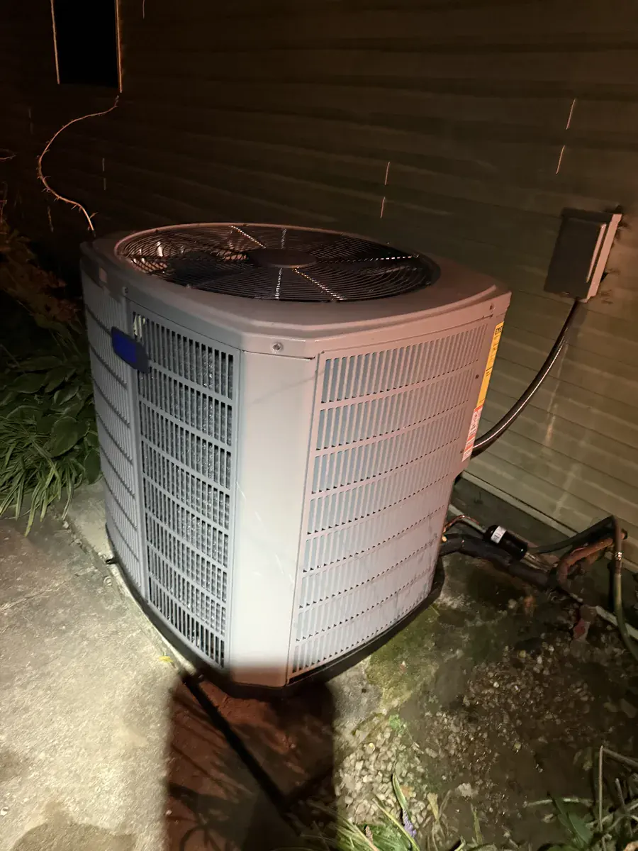 Side view of a new American Standard air conditioner with a power shutoff box on the wall