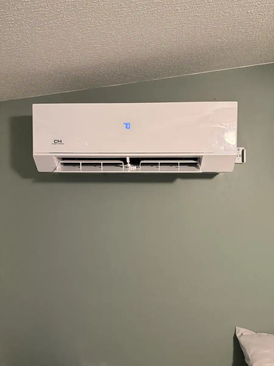 White ductless indoor unit mounted near the ceiling on a green wall