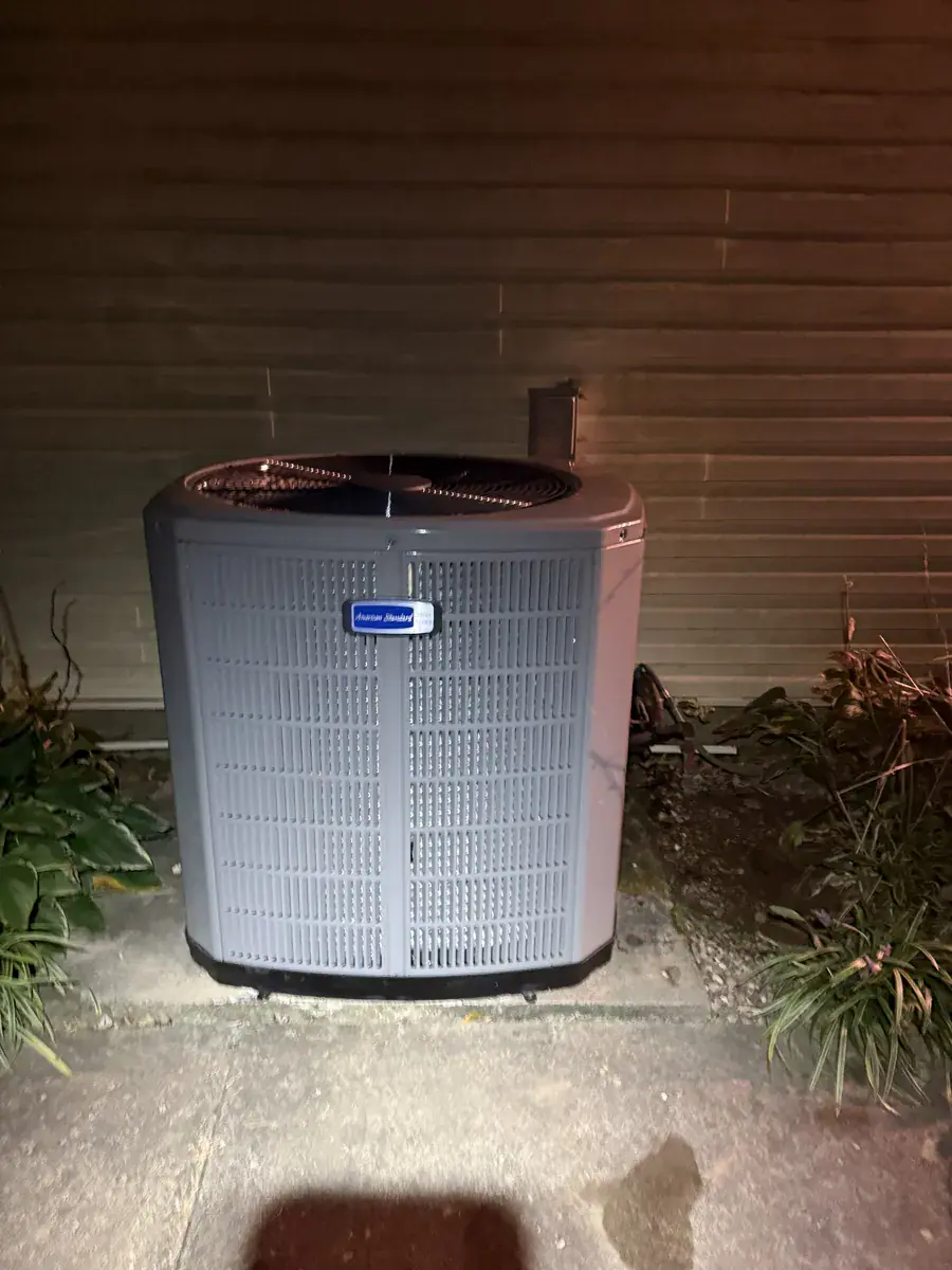 New American Standard air conditioner on a concrete slab beside tan siding