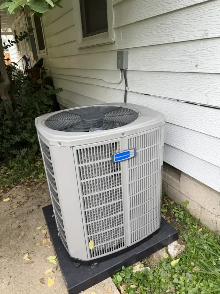 New American Standard air conditioner on a black equipment pad next to white siding