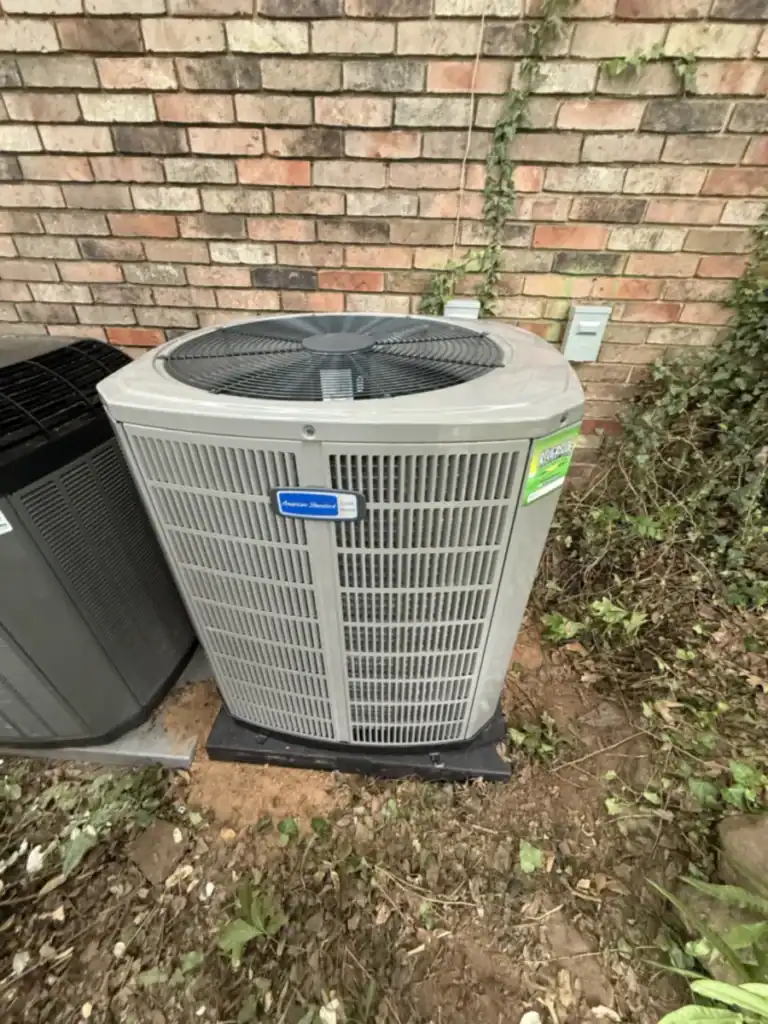 New American Standard Gold air conditioner on a pad beside a brick wall