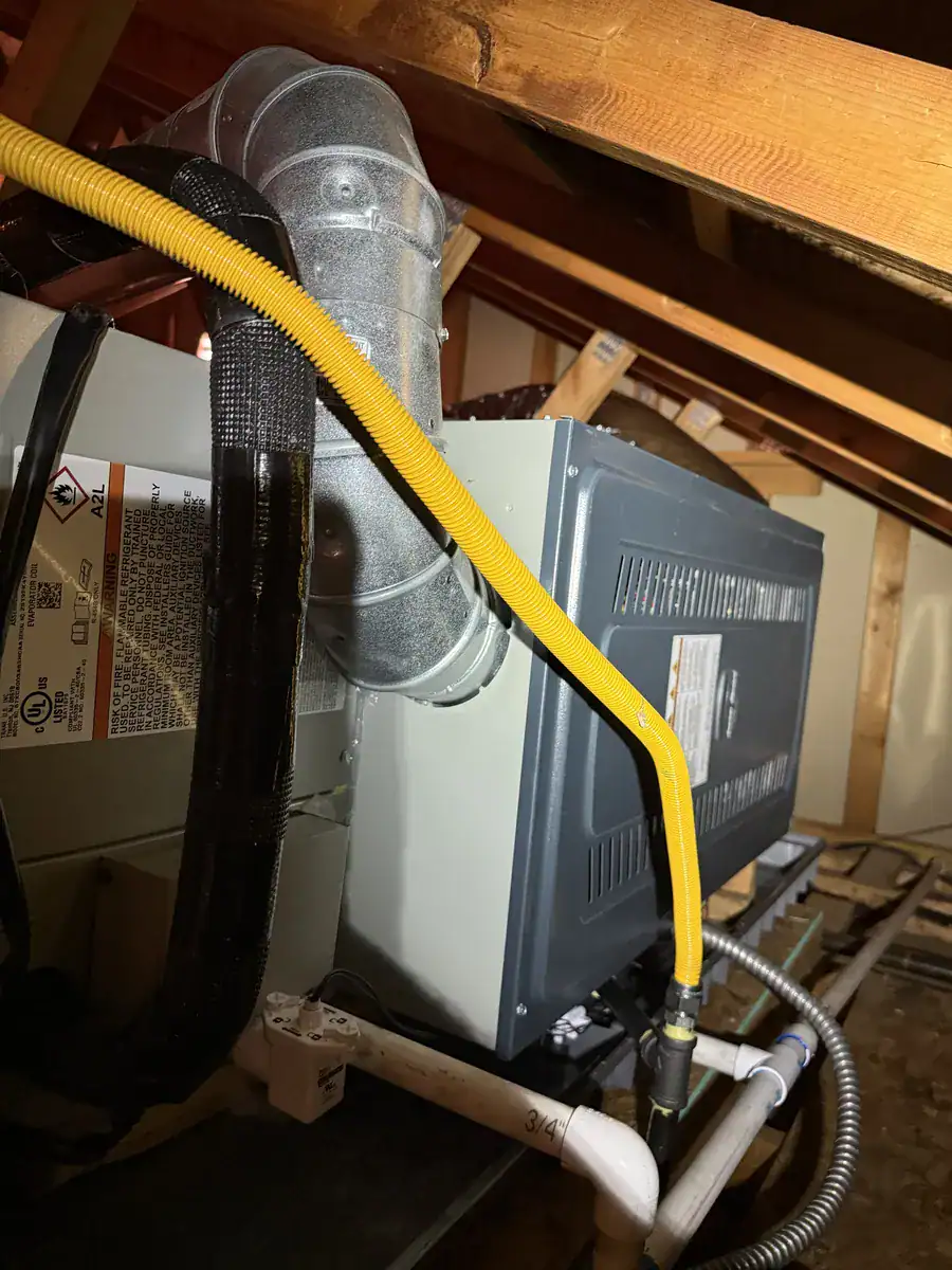 New gas furnace installed in an attic with yellow gas line and white drain pipe