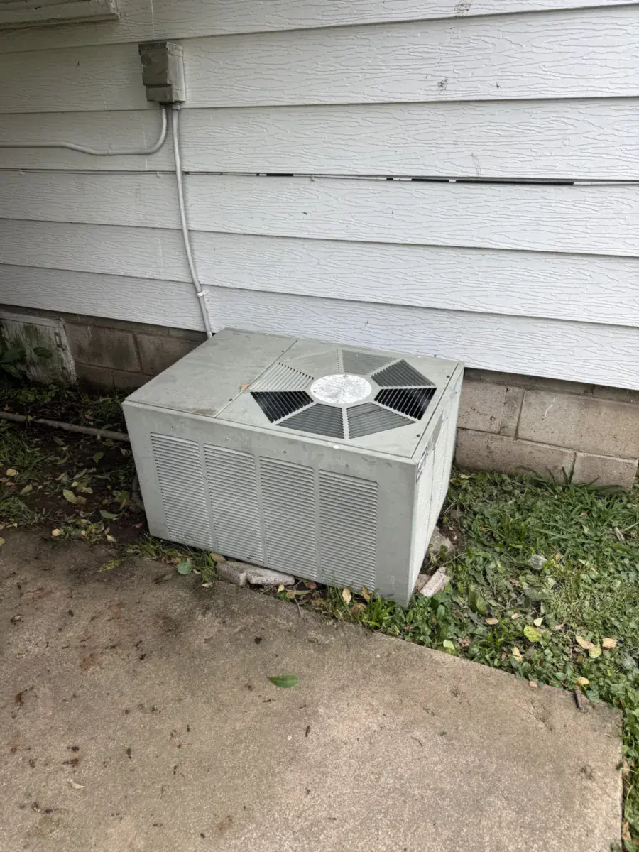 Weathered older outdoor AC unit on a concrete slab before replacement