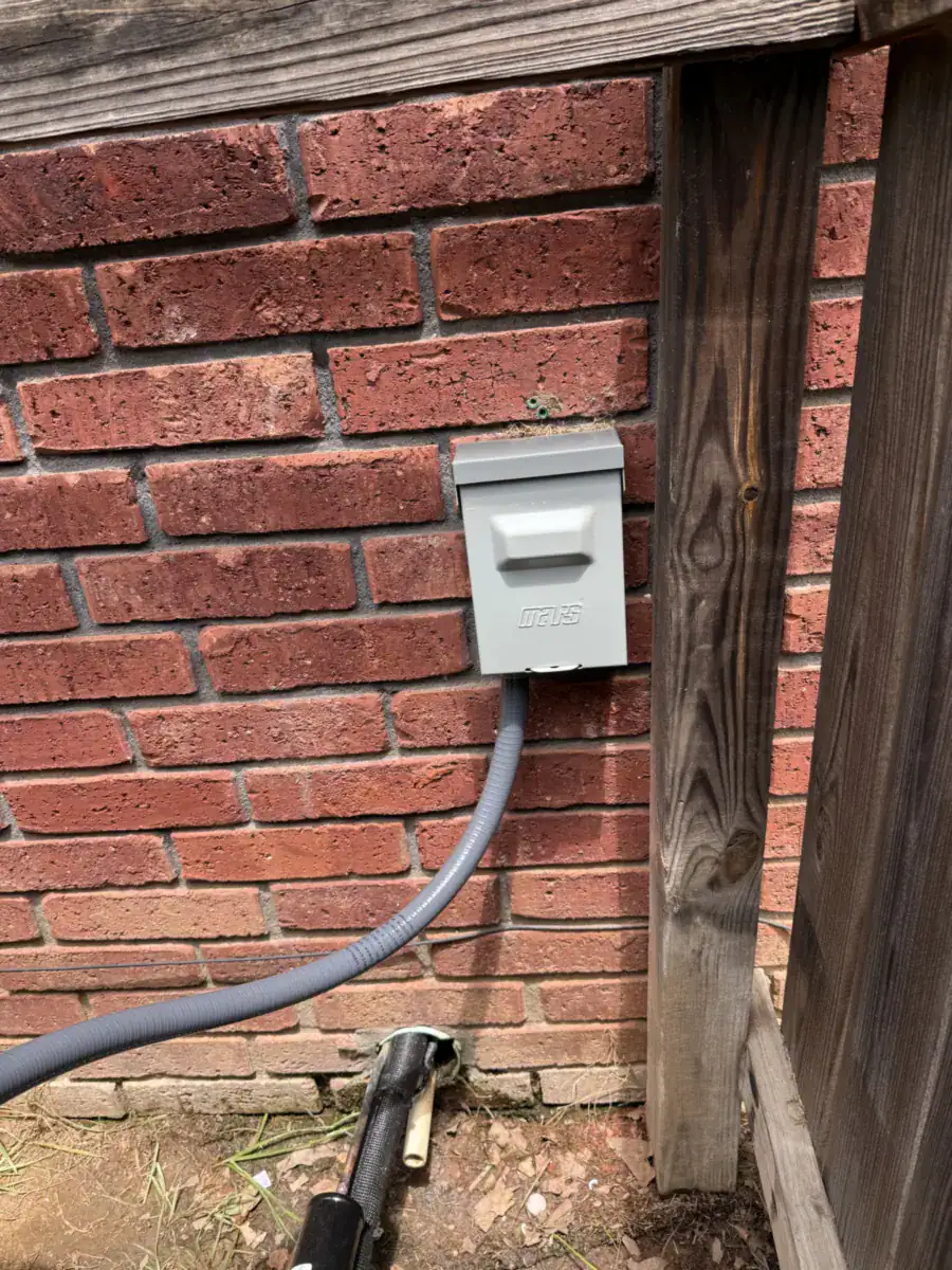 Gray outdoor power shutoff box on red brick with a gray power line running down
