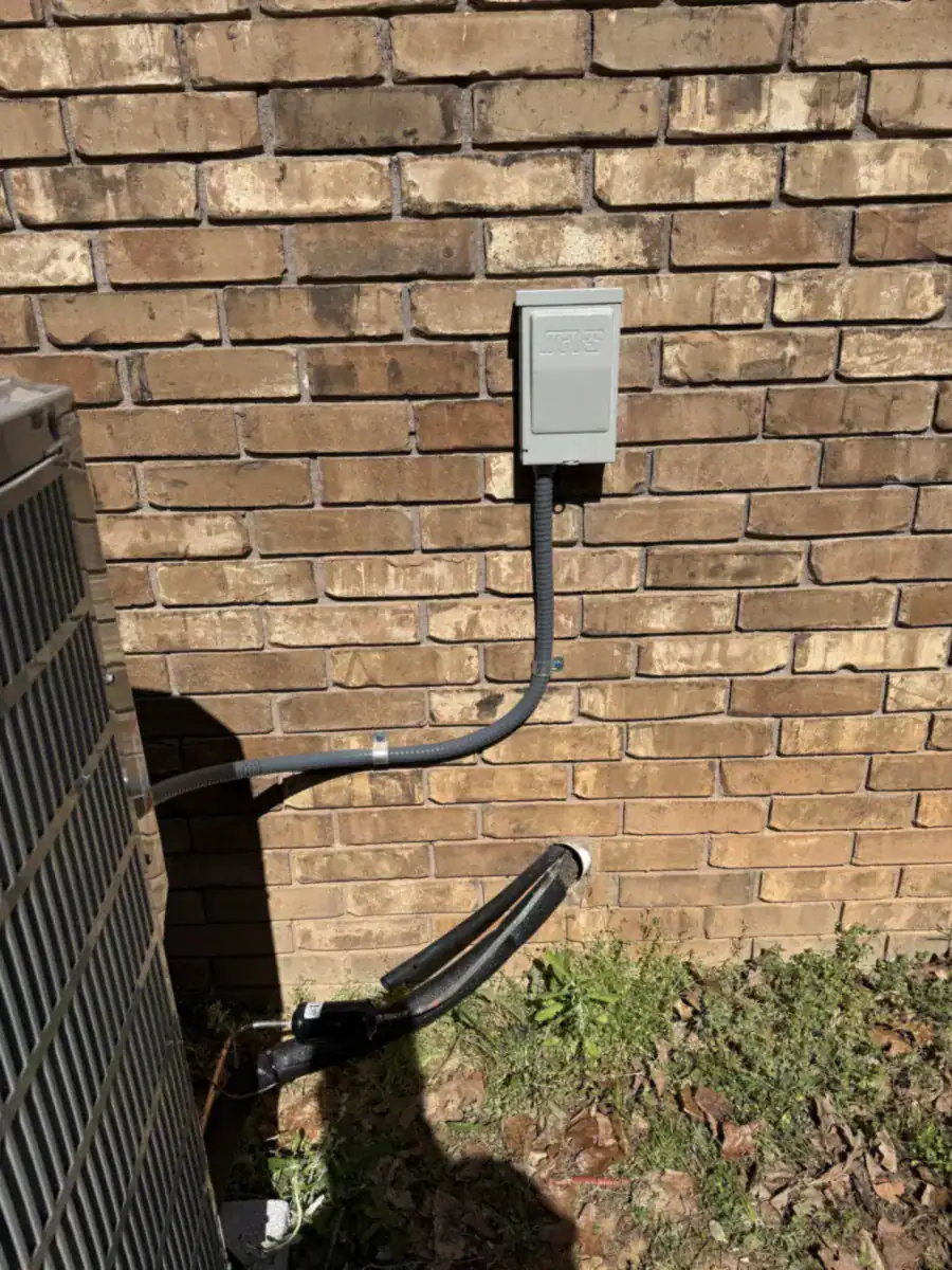 Outdoor power shutoff box on a brick wall with power line running to the AC