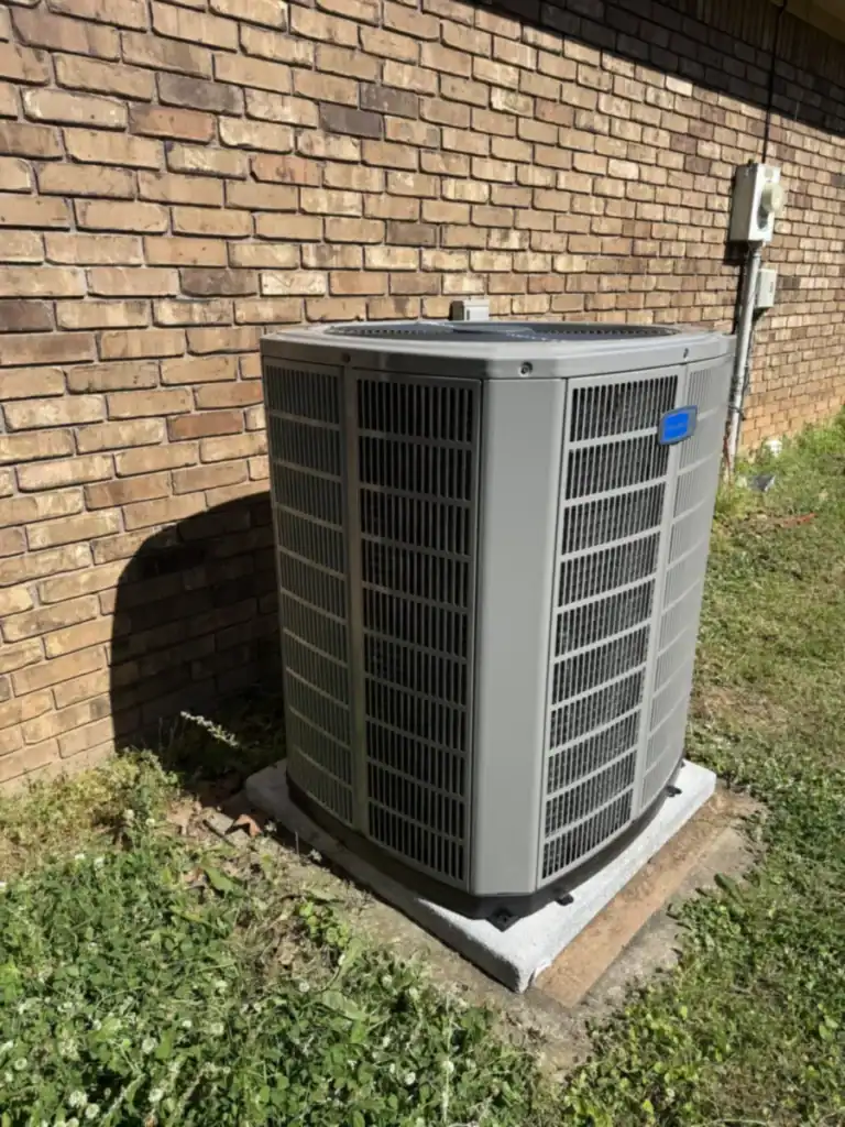 New American Standard air conditioner on a pad next to a tan brick wall