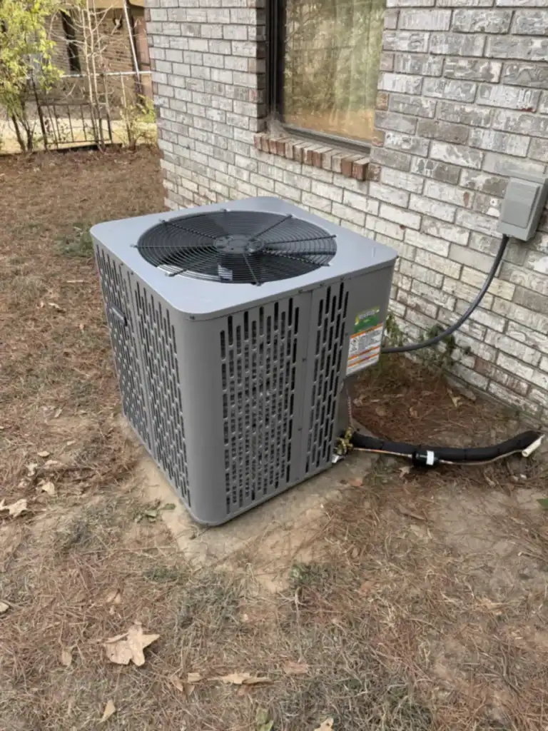New gray heat pump outdoor unit on a slab beside a brick home